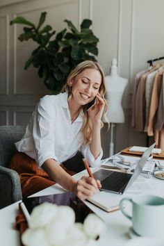 a woman sitting at a desk talking on the phone and working on her laptop computer