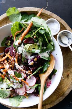 a salad with carrots, radishes and dressing in a white bowl on a wooden platter