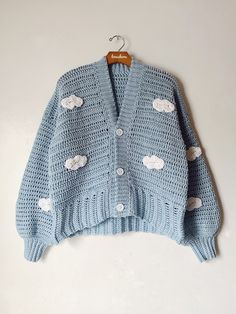 a blue knitted sweater with clouds on it hanging from a wooden hanger against a white wall