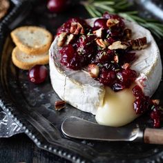 a piece of cheese with cranberry sauce and nuts on top sits on a plate next to crackers