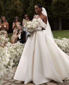 a woman in a wedding dress walking down the aisle with her bridesmaids behind her