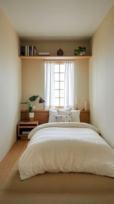 a bed sitting under a window next to a wooden shelf filled with books and plants