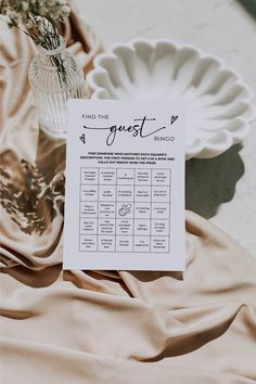 a table with a sign and some flowers on it next to a white plate that says, find the guest