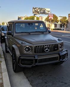 a mercedes g - class is parked on the side of the road in front of some cars