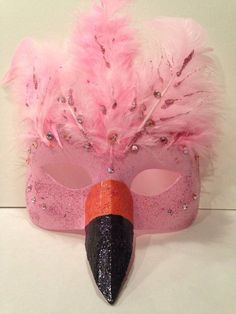 a pink masquerade with feathers on it and a black cone sticking out of the middle