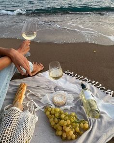 two people are sitting on the beach with wine and cheese