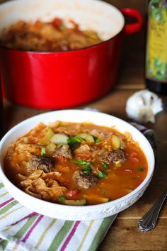 a white bowl filled with meat and vegetable stew next to a red pot full of soup