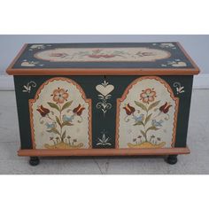 an ornately painted chest on wheels with flowers and hearts in the center, sitting on concrete