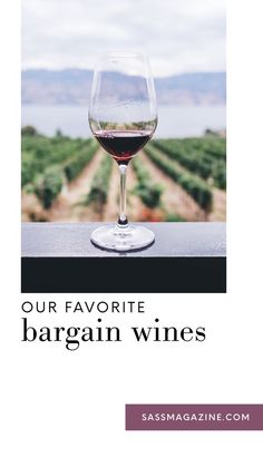 a glass of red wine sitting on top of a table next to a vineyard field