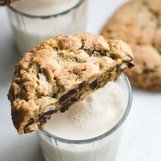 an oatmeal cookie and glass of milk on a white surface with two cookies in the background