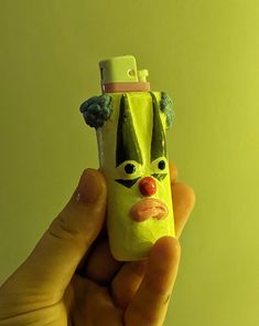 a hand holding a small green object with a face painted on it's side