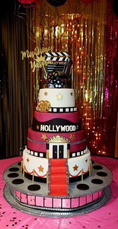 a three tiered cake on top of a pink table cloth with gold and black decorations