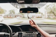 a woman is driving her car and holding the steering wheel with both hands while she holds an object in front of her face