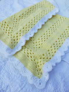 two yellow crocheted blankets sitting on top of a white bed sheet with ruffled edges