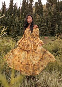 a woman in a yellow dress standing in tall grass with trees in the back ground