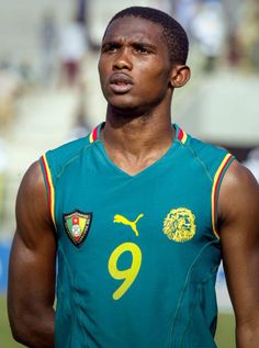 a young man wearing a green and yellow uniform standing in front of a soccer field