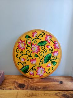 a yellow plate with pink flowers painted on it sitting on a wooden shelf next to a brick