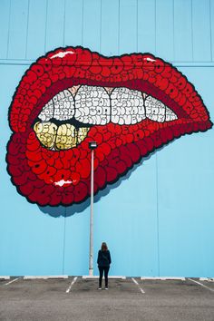 a person standing in front of a blue wall with a large red lips painted on it