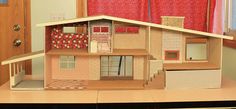 a doll house sitting on top of a table next to a red curtained window