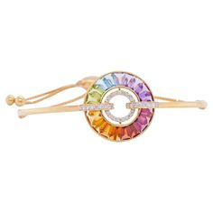 18 karat gold channel set rainbow baguette gemstones diamond circle bolo bracelet This bracelet is a radiant celebration of color and elegance. Crafted with meticulous precision, this bracelet features a stunning arrangement of vibrant rainbow gemstones, including blue topaz, amethyst, citrine, peridot, garnet, rhodolite, and iolite, taper cut to perfection. Each gemstone is carefully set in a channel setting, forming a mesmerizing circle of captivating hues. Interspersed among the gemstones are sparkling diamonds, adding a touch of brilliance and sophistication to the design. The bolo style of the bracelet allows for easy adjustment, ensuring a comfortable and secure fit on any wrist. Whether worn alone as a statement piece or layered with other bracelets for a bolder look, this bracelet Luxury Fine Jewelry Multicolor Bangle, Luxury Rainbow Bracelet Jewelry, Luxury Rainbow Colored Fine Jewelry Bracelet, Rainbow Sapphire Bracelet, 14k Gold Rainbow Multi-stone Jewelry, Rainbow Gemstones, Circle Diamond, Diamond Settings, Baguette Diamond