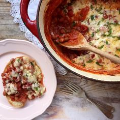 a white plate topped with pizza next to a red pot filled with sauce and cheese