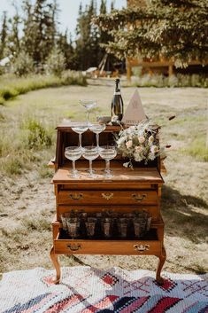 an old dresser with wine glasses and flowers on it is sitting in the middle of a field