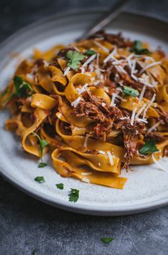 pasta with meat and parmesan cheese on a white plate, garnished with parsley