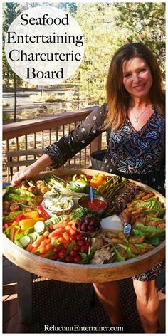 a woman holding a tray full of food on top of a wooden deck with the words seafood entertaining charcuterie board