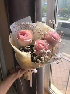 a bouquet of pink roses sitting on top of a window sill next to a person's hand