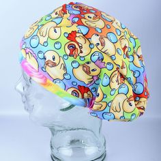 a multicolored surgical cap with rubber ducks on the front and sides, sitting on a head mannequin