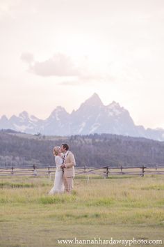 a bride and groom standing in a field with mountains in the background