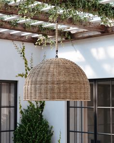 a wicker light fixture hanging from a wooden pergolated ceiling over a patio