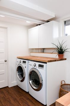 a washer and dryer in a white laundry room with wooden counter top on the floor