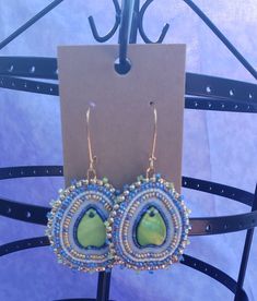 Green shell center with clear, blue, and gold beads. Another very simple design that looks amazing and complex with the addition of the gold beads and the shape of the shell. The slightly inward curve of the shell also adds to that, making it so much more then what you see. Bohemian Embellished Beaded Earrings, Bohemian Adjustable Embellished Jewelry, Teardrop Beaded Jewelry For The Beach, Beaded Teardrop Jewelry For The Beach, Artisan Blue Jewelry With Gold Beads, Blue Beaded Earrings With Gold Beads For Festivals, Handmade Teardrop Bohemian Beads, Artisan Blue Jewelry With Bead Caps, Bohemian Embellished Earrings For Gift