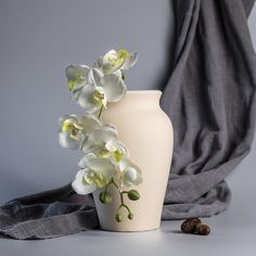 a white vase with flowers in it sitting next to a gray cloth on the floor