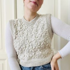 a woman wearing a white sweater and blue jeans with her hands on her hips, posing for the camera