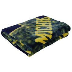 a blue and yellow blanket with the word michigan on it, folded up in front of a white background