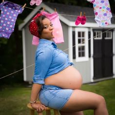 a pregnant woman is sitting on a chair with clothes hanging from the line above her head