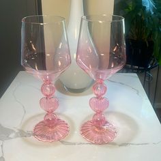 two pink glass goblets sitting on top of a white countertop next to a vase