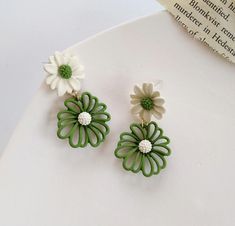 green and white flower shaped earrings on top of a piece of paper next to a book