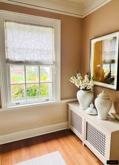 a vase with flowers is sitting on a shelf in front of a window and framed pictures