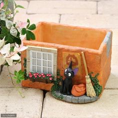 a cat figurine sitting on top of a potted planter next to a window