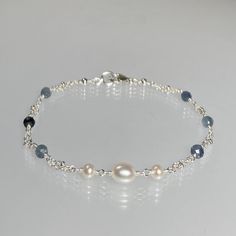 Genuine shaded blue sapphire gemstone and freshwater pearl, wire-wrapped sterling silver bracelet. This dainty bracelet is designed with a single white oval pearl, 2 small semi-round pearls and genuine premium-quality, ombre blue sapphire gemstones, evenly spaced along sterling silver double-strand chain. The pearls are positioned in the centre of these rondelle-shaped gemstones; which are micro-faceted, and highly polished.  This bracelet is completed with a sterling silver lobster-claw clasp. This simple and feminine bracelet, with shades of blue, drapes beautifully and is suitable for any occasion ! Sapphire is the birthstone for September and pearl for June.   A dainty bracelet that is enlarged to show details.  Details: *  length: please choose at check-out genuine faceted ombre blue Silver Dainty Jewelry, Elegant Blue Beaded Bracelets With Pearl Charm, Handmade Adjustable Blue Pearl Bracelet, Adjustable Blue Pearl Bracelet With Gemstone, Elegant Handmade Blue Pearl Bracelet, Elegant Blue Pearl Bracelet With Charm, Sapphire And Pearl, Feminine Bracelet, Bracelets Pearl