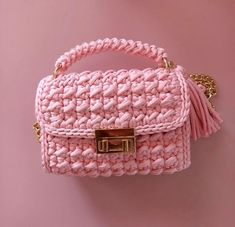 pink crocheted purse with gold hardware and tassels on the handle, against a pink background