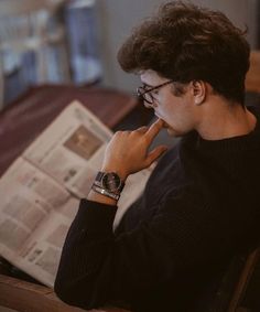 a man sitting at a table reading a newspaper while holding his hand to his face