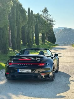 a black sports car parked on the side of a road next to some tall trees