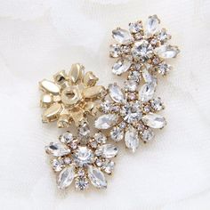 two pieces of brooch and ear clips on a white cloth covered surface with flowers in the center