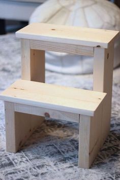 a small wooden step stool sitting on top of a table next to a white vase