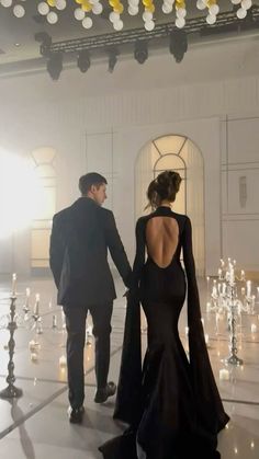 a man and woman in formal wear walking down a hall with candles on the floor