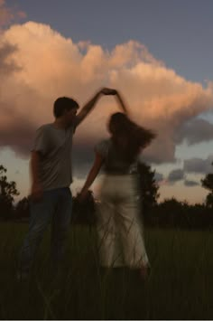 two people standing in the grass with their arms around each other and one person reaching for something